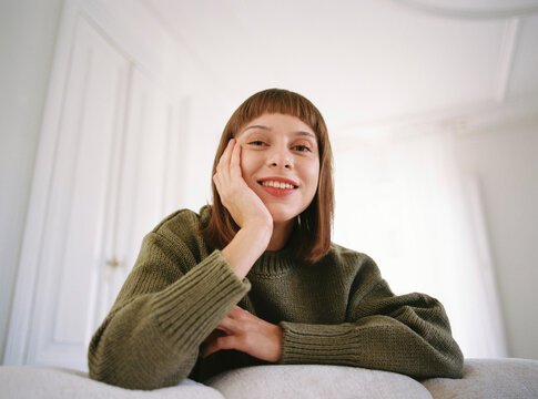 Smiling woman looking at camera while resting on white sofa