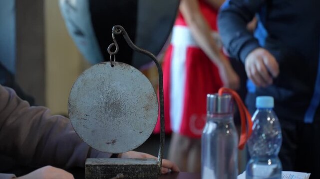Close up of a traditional metal gong on a table with water bottles and athletes in the background, martial arts competition, sport event atmosphere