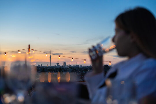 Young woman drinking wine on a rooftop terrace with a view of Berlin