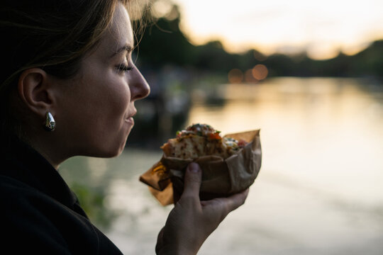 Young woman eating a sandwich with a lake view during sunset