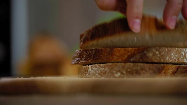 Hands stack freshly sliced whole grain bread on a wooden table. Warm loaf with a crisp golden crust in a real bakery setting, simple farm-grown grains and everyday artisan baking.