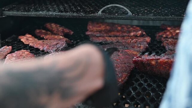 Meat is placed on a grill in an outdoor setup. Stainless steel tongs are used to manage the grilling process.
