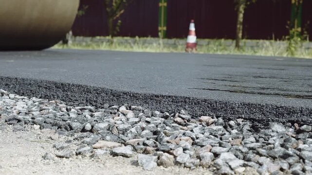 A road roller levels and compacts fresh asphalt as construction machinery builds a new road in a small town. Workers repair and smooth the surface, supporting city growth and infrastructure developmen
