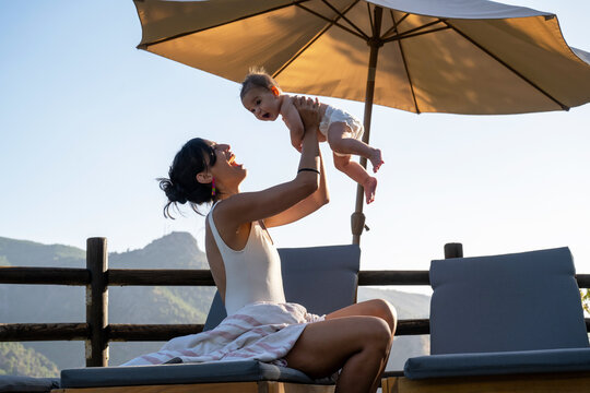 Woman Lifting Baby With Joy On Deck Chair