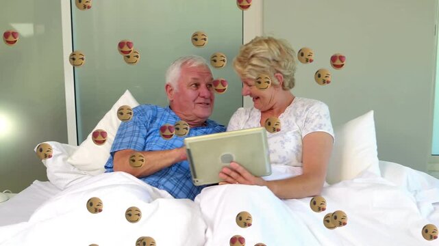 Animation of face emoji icons floating over caucasian senior couple using laptop in the bed