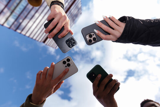 Cropped bottom of friends hands holding different cellphones outdoors