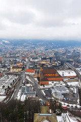 Fototapeta premium Aerial view of Innsbruck, Austria, under winter overcast. Wiltener Basilica and monastery stand near rail lines and a cemetery. Rails and roads thread toward the center.
