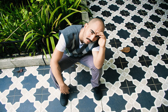 Man Posing Thoughtfully on Patterned Tiles in a Garden Setting
