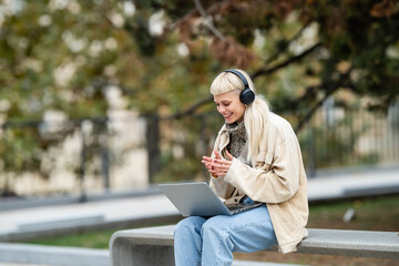 Obraz premium Woman having video call in park with laptop and headphones