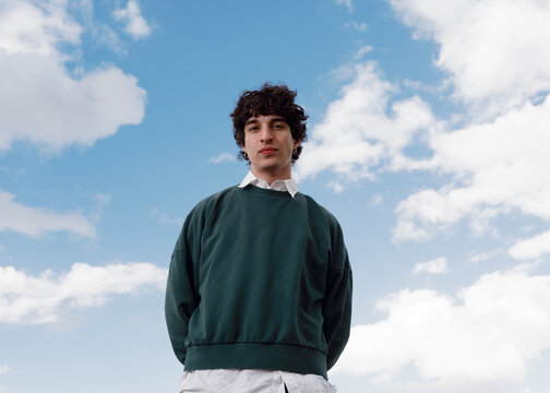 Teenager Stands Confidently Outdoors Under a Blue Sky With Clouds