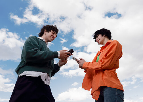 Friends Sharing Phone Screens Under a Blue Sky With Clouds
