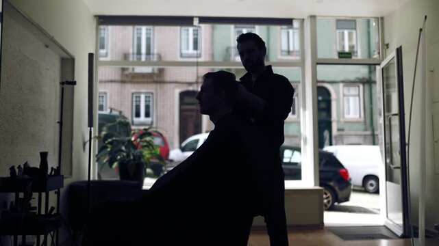 Hairdresser styling customer's hair in barbershop silhouette