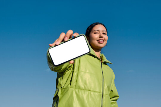 Person holding smartphone with blank screen under blue sky