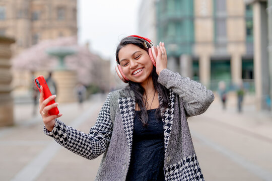 Woman enjoying music while walking on a city street during a cloudy day in spring