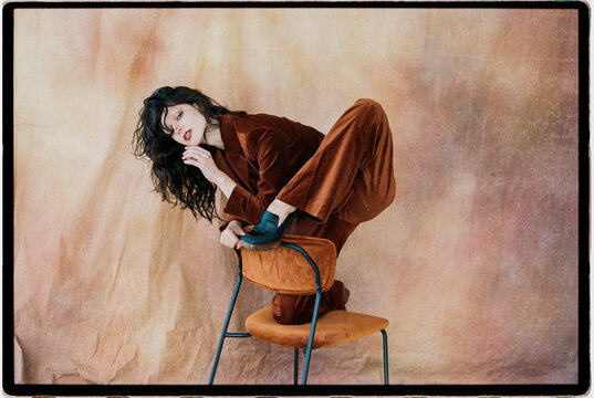 Woman in velvet suit posing creatively on chair
