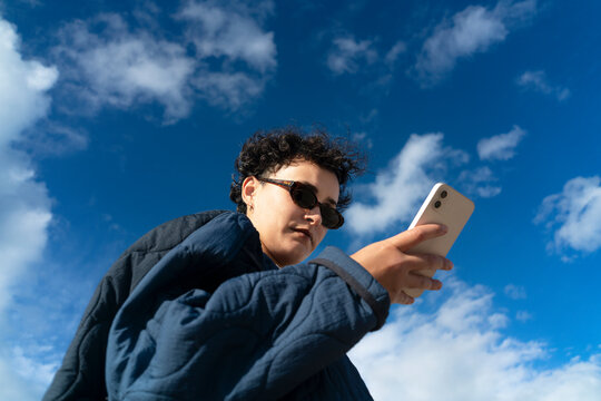 Casual woman using phone against blue sky with white clouds