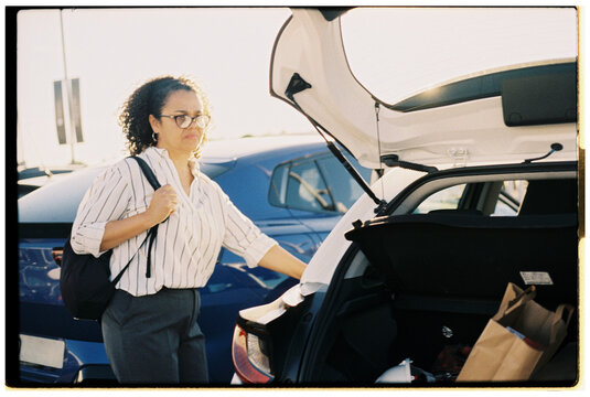 Woman Loading Groceries Into a Car at Sunset in a Parking Lot