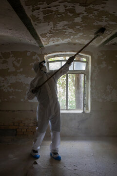 Worker Removing Old Paint in a Dilapidated Room