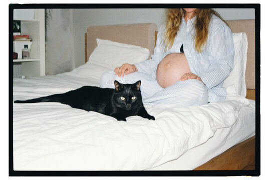 Expecting a baby while relaxing with a black cat on the bed 