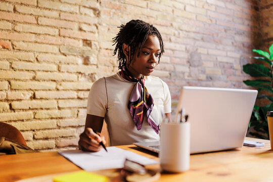 Woman working on laptop and writing notes at office