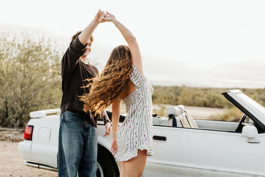 Young couple twirling in front of convertible 