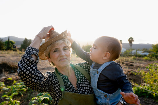 Grandmother holding baby grandson playing with hat