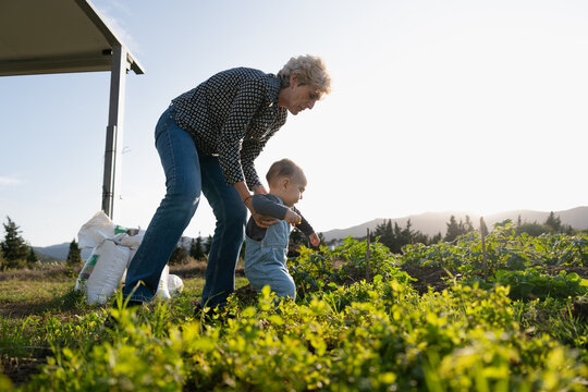 Grandmother helping baby grandchild walking in garden