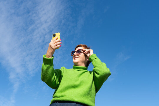 Joyful woman taking selfie in vibrant green sweater under blue sky