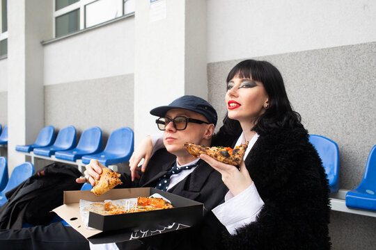 A man and a woman are eating pizza on stadium chairs.