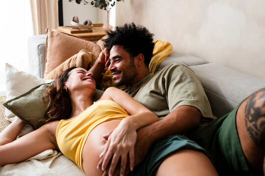 Cheerful pregnant couple having fun on sofa
