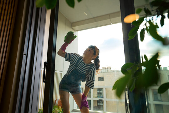 Woman cleaning apartment window with rubber gloves
