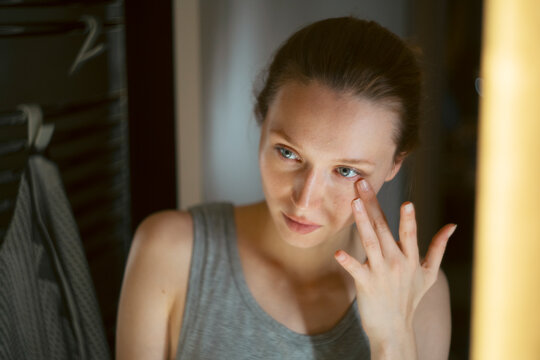 Woman applying eye cream in mirror at night
