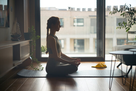Woman meditating in lotus pose practicing mindful yoga at home
