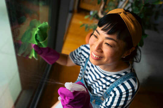 Asian woman cleaning window, enjoying daily home chore