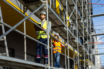 Male and female engineers walking on scaffolding to inspect construction site progress.