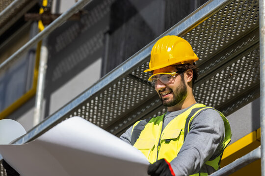 Portrait of a young male engineer holding an open blueprint on a construction site.