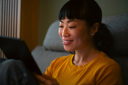 Asian woman smiling using tablet relaxing at home