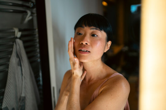 Asian woman applying cream on face in bathroom