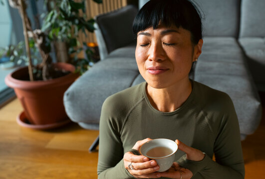 Woman meditating and relaxing with calming tea at home
