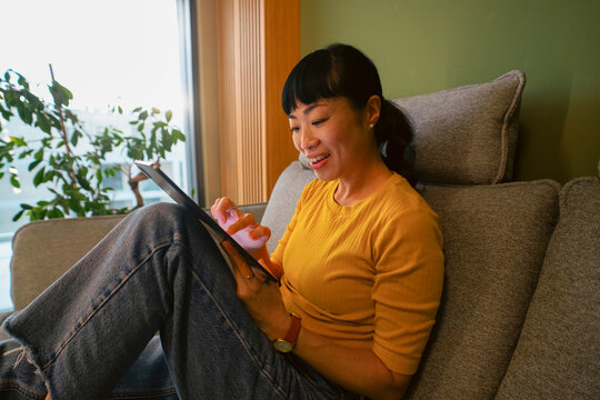 Woman relaxing at home using digital tablet on sofa