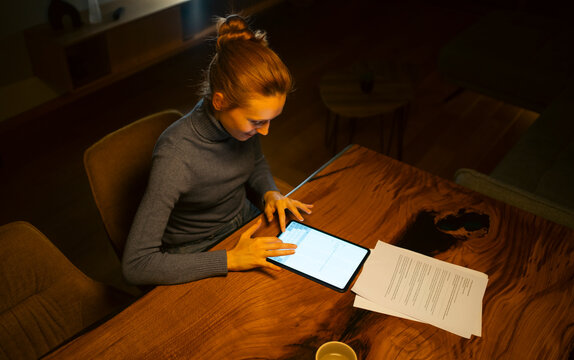Woman working late on tablet with documents at home