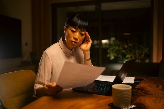 Woman feeling stressed reviewing documents at night home office