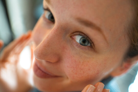 Woman with freckles applying skincare for natural beauty
