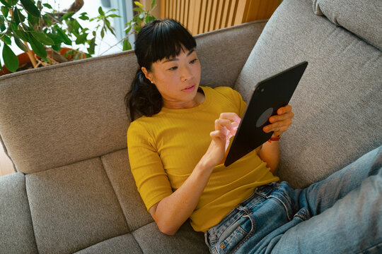Woman relaxing on couch using digital tablet at home

