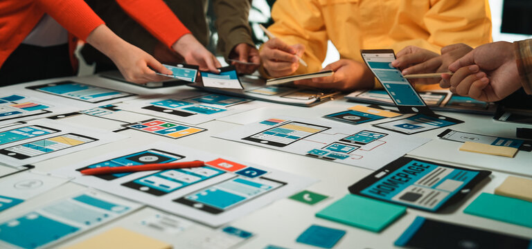 A diverse team engages in a dynamic design session, crafting wireframes and prototypes for mobile and web applications on a collaborative table filled with digital devices. SACTR