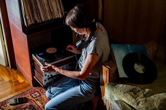 Young modern woman putting vinyl record on record player to listen