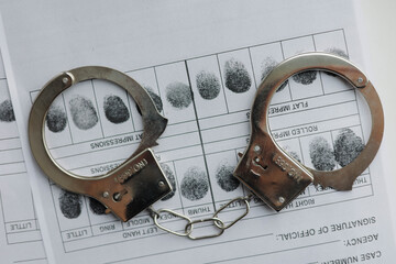 Handcuffs and fingerprints card on the white table. Crime investigation concept.