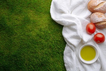 Naklejka premium Bread rolls tomatoes and olive oil on white towel next to grass background, copy space