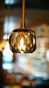 Close up of amber faceted glass pendant light in restaurant. Modern amber glass lamp with geometric texture hanging indoors against blurred background.