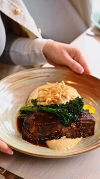 Person holding plate of braised beef with mashed potatoes. Close up of female hands holding ceramic dish with slow cooked meat and vegetables.